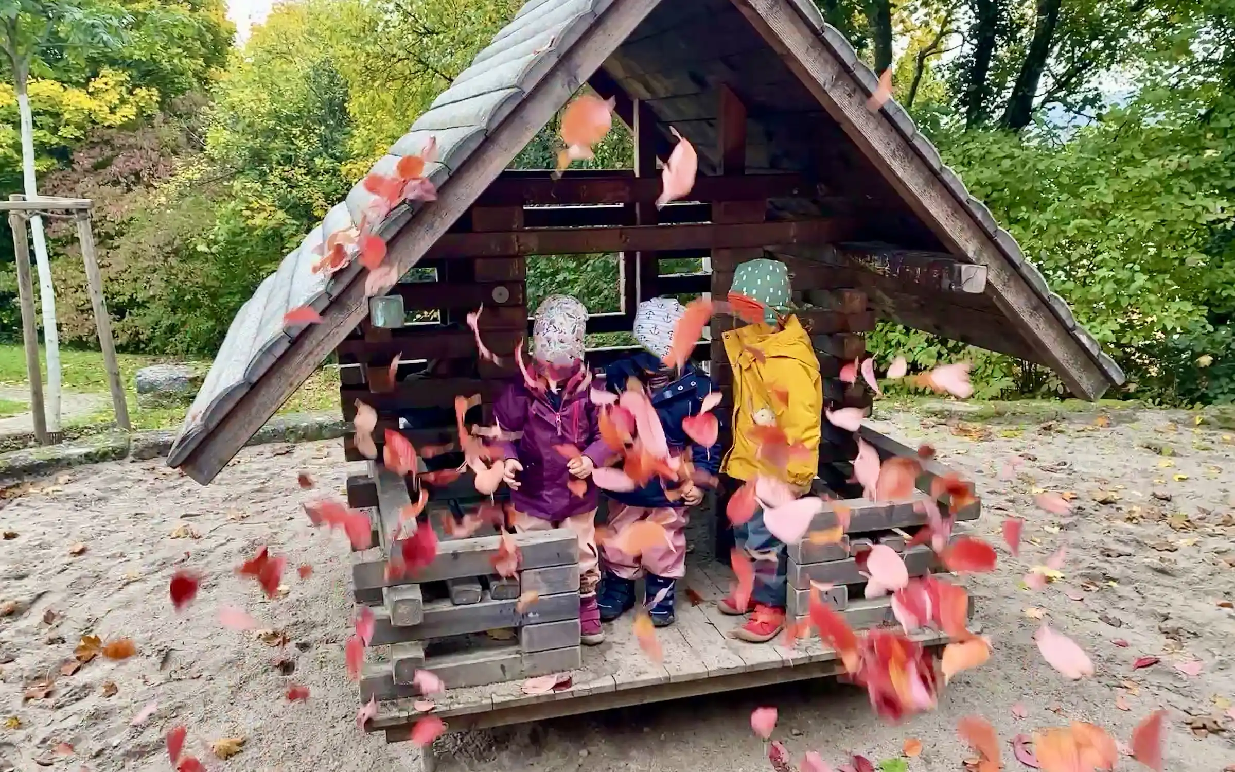 3 Kinder auf dem Spielplatz Egerweg im Spielhaus und fliegenden Herbstblättern