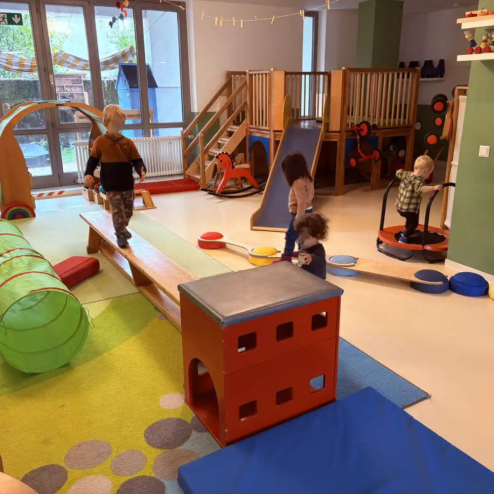 Kinder erkunden im Gruppenraum einen kleinen Parcours zum Klettern und für die Geschicklichkeit.
