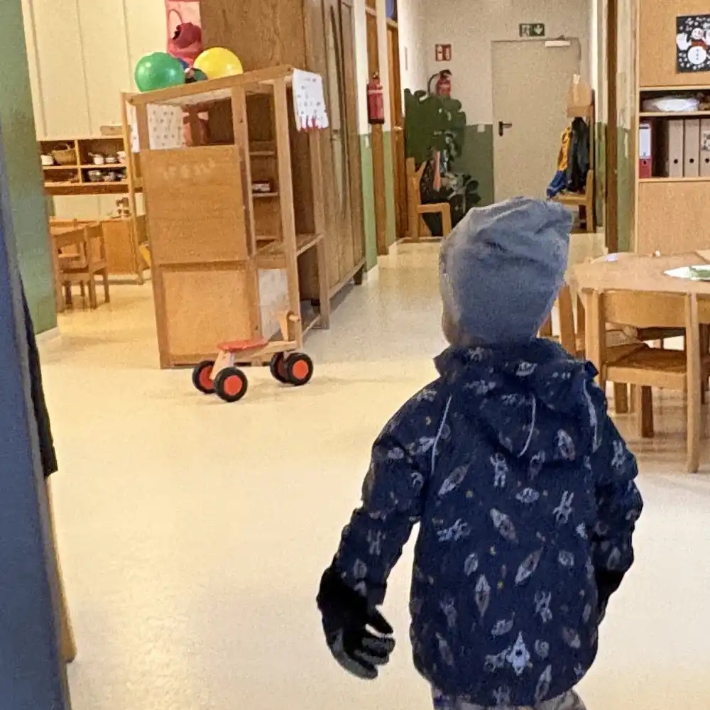 Ein Kind betritt den Eingang zur Kita und schaut sich neugierig um.